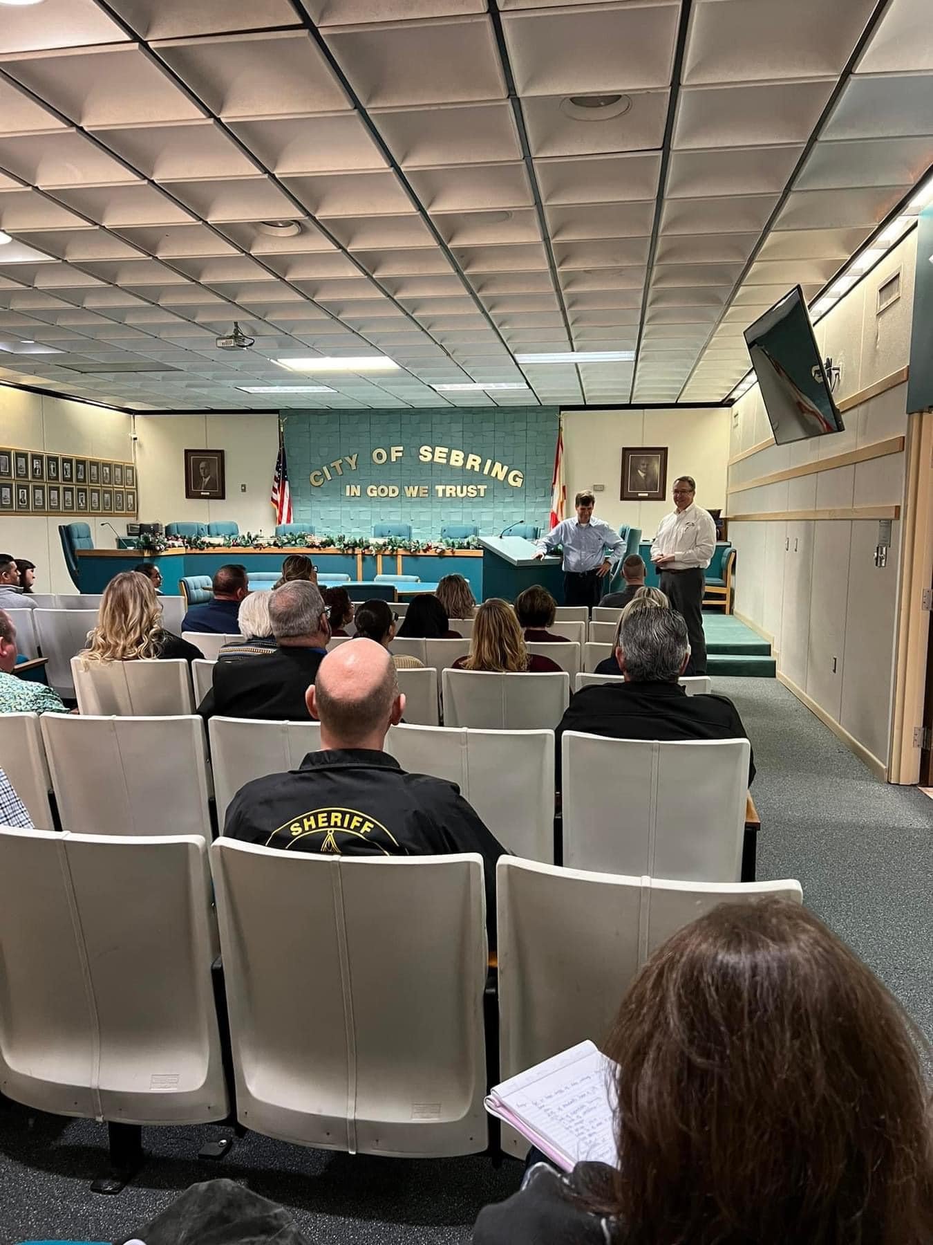 Group sitting in City of Sebring meeting room with two men speaking at front of room