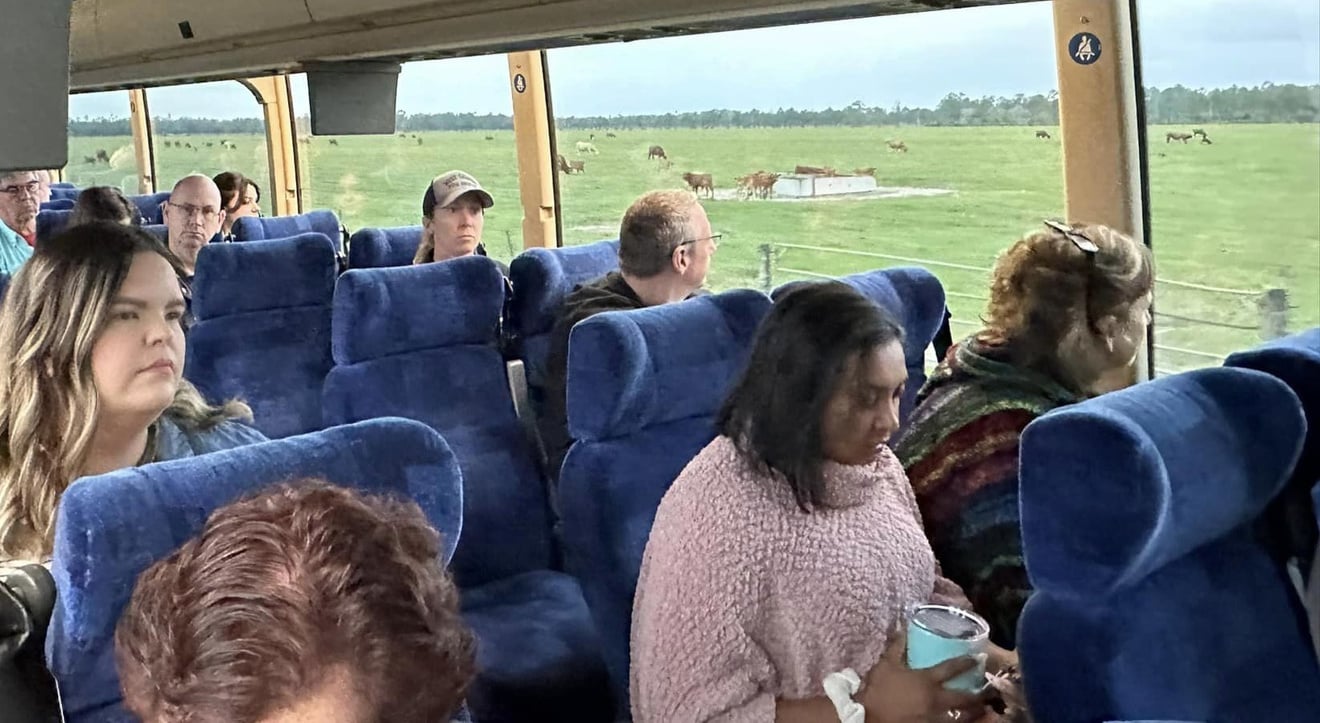 Class members riding a bus with cows visible outside windows