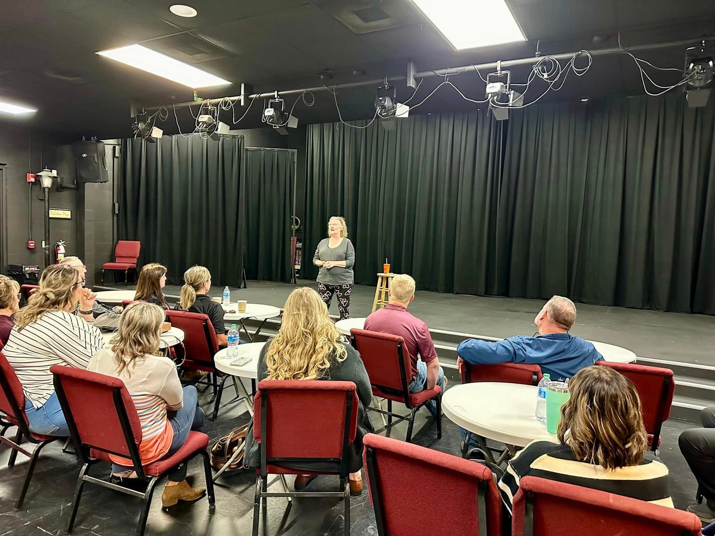 Group sitting in a theater with a woman speaking onstage